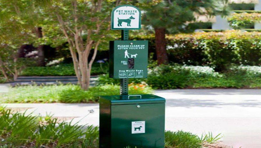 A pet waste station installed in a well-maintained park, featuring a sign and waste disposal bin for responsible pet waste management.